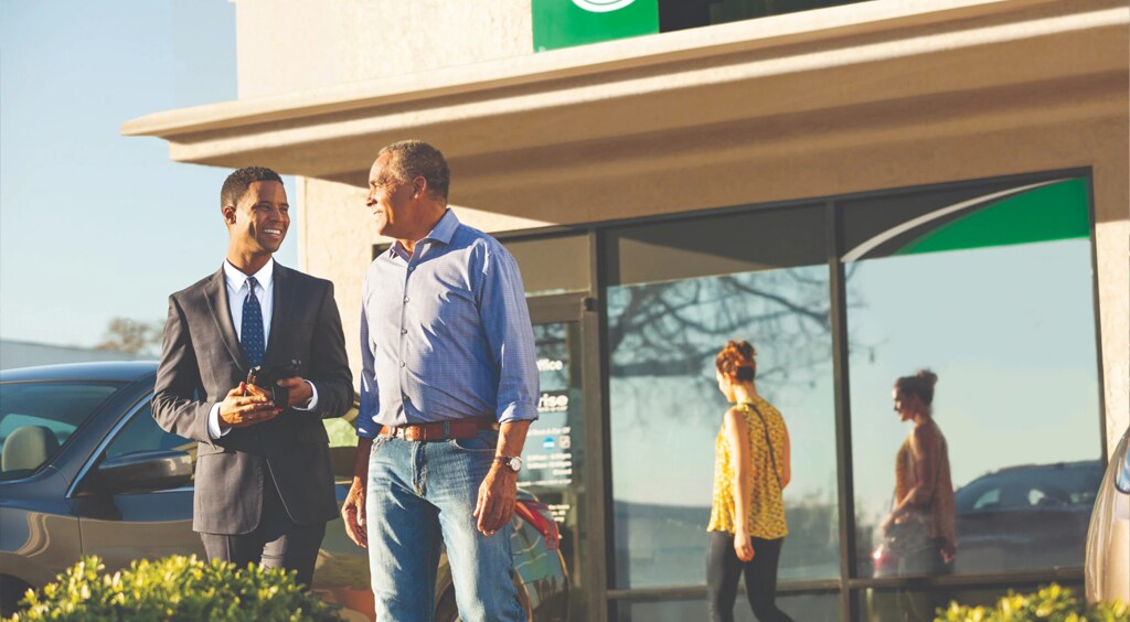 two men standing outside car rental building